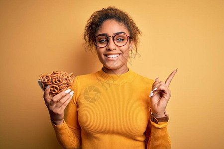 非洲裔美籍女孩在黄色背景上拿着德国烤面包饼的碗包图片