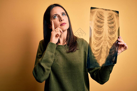 蓝眼睛的棕发年轻女人在黄色背景上对肺部进行X光检查严肃地思考问题图片
