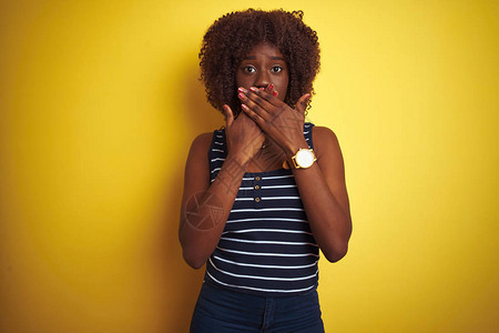 身穿T恤的非洲年轻女在孤立的黄色背景上被用双手遮住嘴顶大惊小怪图片