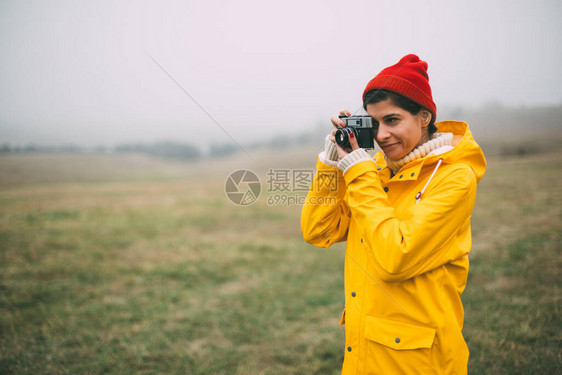 年轻登山摄影师在雨天享受拍摄雾风景穿着黄色雨衣的笑女人图片