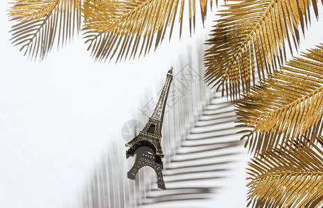 简约时尚静物埃菲尔铁塔雕像在白色背景上的装饰棕榈叶中棕榈叶的图片