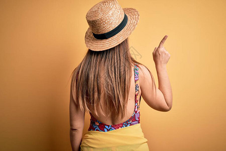 黄色背景中身穿泳衣和夏帽的年轻金发美女用手指图片