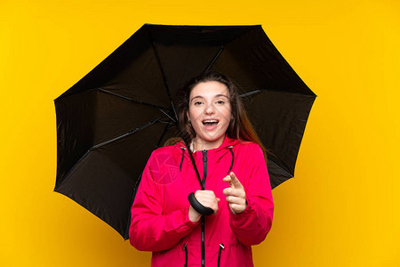棕发年轻女孩拿着雨伞在孤立的黄色背景上大吃一图片