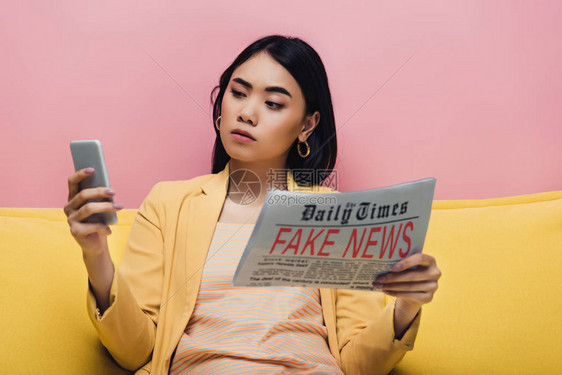 带着假新闻和智能手机的报纸站在粉红色孤立的黄色沙发上图片