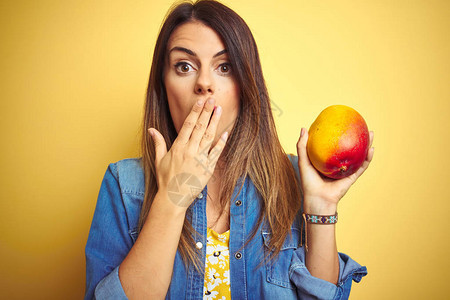 美丽的年轻女子在黄底面的嘴唇上吃新鲜健康芒果图片