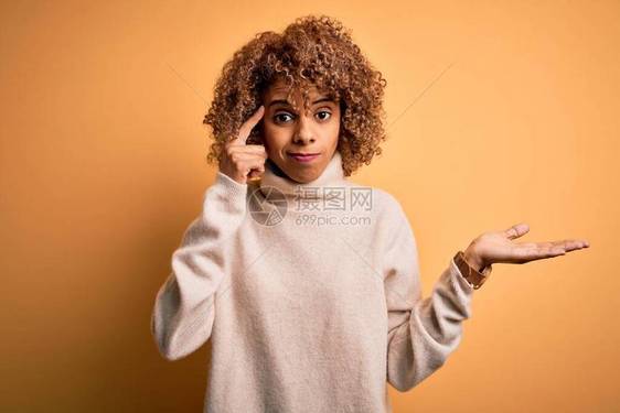 年轻美丽的非洲女穿着黄皮毛衣在黄色背景中迷惑不解图片