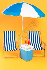 沙滩雨伞附近的甲板椅子和黄色的便携式冰箱冷图片
