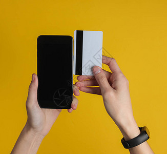 手与智能手镯持有银行卡和智能手机在黄色背景图片
