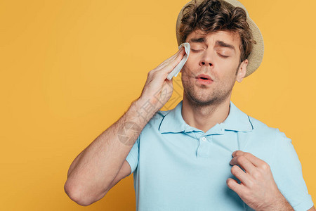 汗流浃背的男人用黄色隔离的餐巾擦脸图片