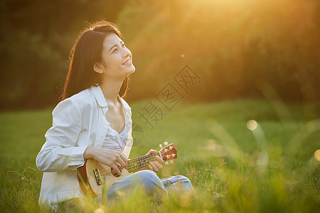 阳光下的美女坐在草地上弹吉他图片