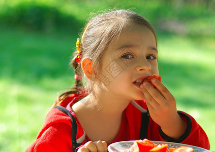 小女孩坐在花园里的餐桌旁吃着西红柿图片