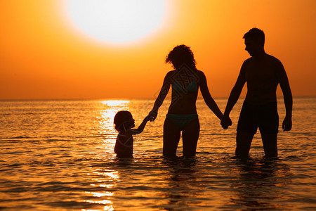 日落时带着孩子在海里的父母图片