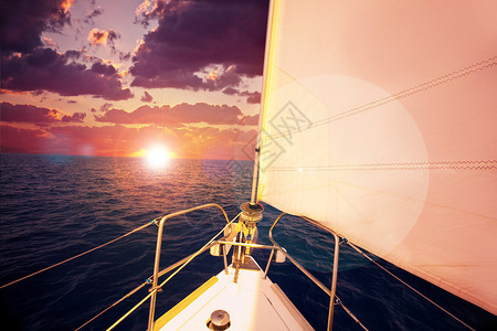 浪漫的日落和帆船紫色云彩的戏剧天空和平静的海面上的太阳耀斑水上运动旅图片