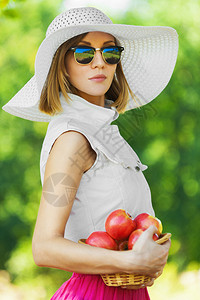美丽的年轻女孩的肖像严肃的帽子拿着篮子苹果在夏季图片