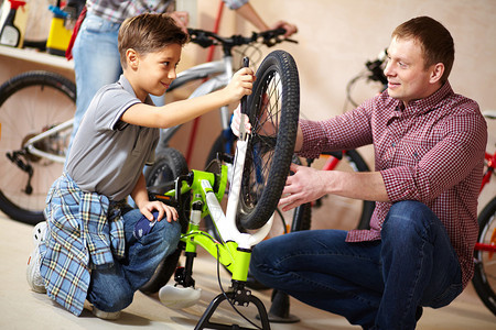 可爱男孩的肖像在修自行车轮他的父图片