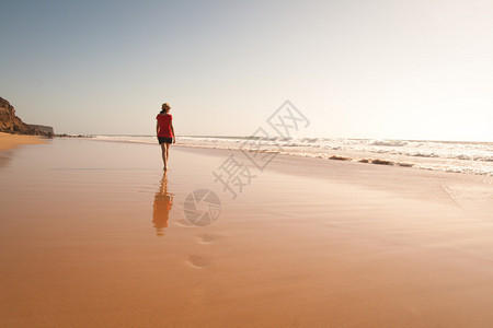 孤单的女孩走在孤独的沙滩上与她的反射图片