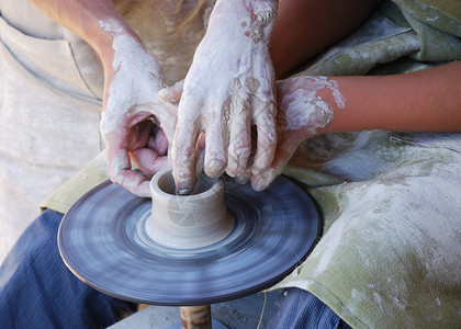 一个学徒正在用飞轮制作陶器他得到了师傅的帮助在照片中图片