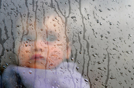 一个小婴儿透过窗户看雨背景图片