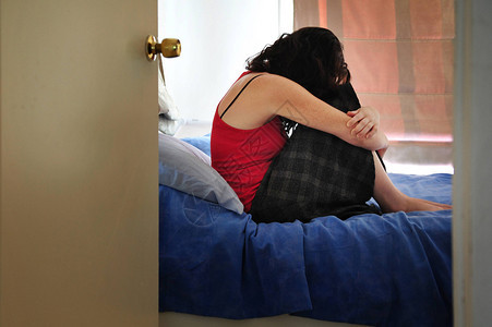 坐在家中卧床上的情绪压抑的年轻女患图片