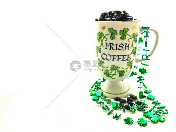 爱尔兰咖啡杯与棕色咖啡豆和绿色三叶草在圣帕特里克节的孤图片