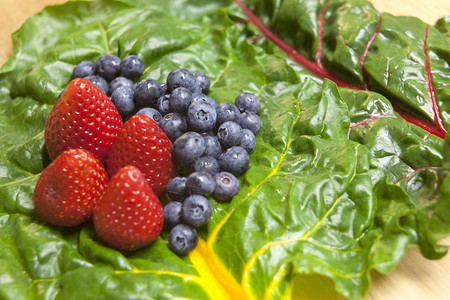 草莓和蓝莓展示在彩虹甜菜的叶子上图片