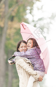 美丽的母亲在伞下拥抱女儿在雨天微笑的女人和女孩快乐妈和孩子的画像图片