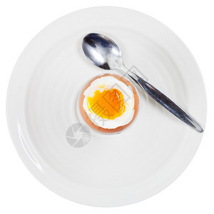 鸡蛋杯中软煮鸡蛋的顶部视图和白盘上的勺图片