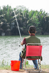 一位资深渔民坐着抓鱼的后视图图片