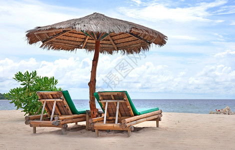 在白沙滩上用竹阳伞看着海洋和蓝天空的舒图片