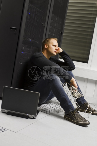 在数据中心的工程师顾问坐在服务器机架前坐着冷酷无情的坐姿图片