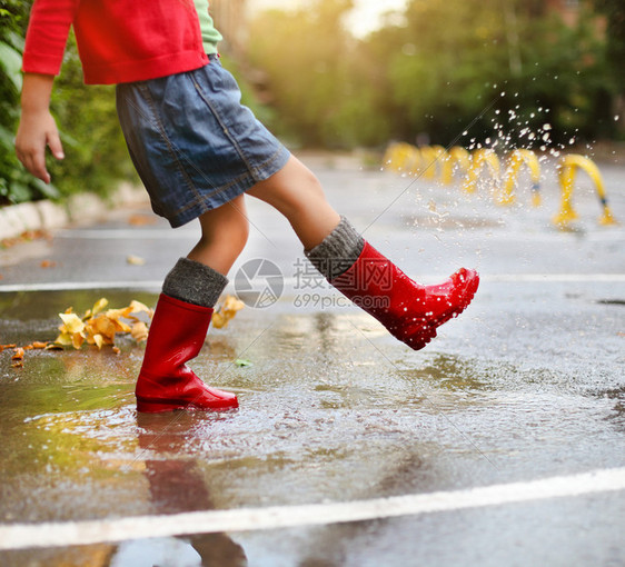 穿红色雨靴的孩子跳进水坑特写图片