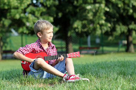 男孩坐在草地上弹吉他图片