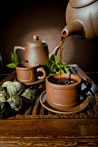 棕色背景的杯子中的粘土茶壶水图片