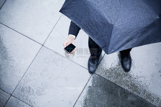 高角度观望着持有雨伞在雨中看手机的商人图片