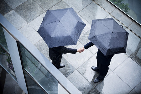 两名持雨伞和握手的商人的高角度视野图片