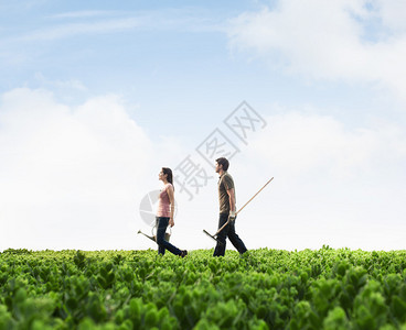 两名青年携带园艺设备步行穿过绿色田地图片