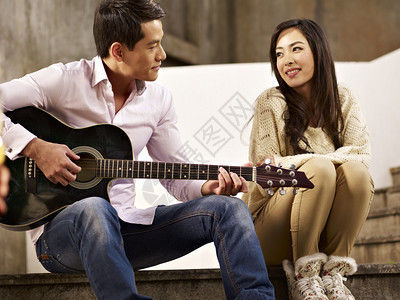 年轻的亚洲情侣坐在弹吉他和图片