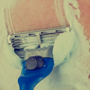 一个用剃须霜或泡沫刮胡子的人在脸上刮胡须碎块的剃刀图片