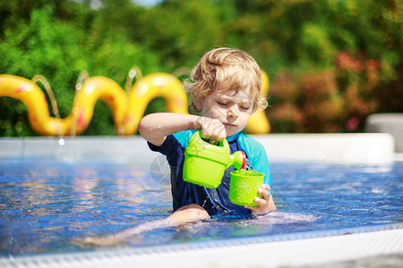 3岁穿保护泳衣的可爱男孩在户外游泳池里玩图片