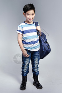 小亚洲孩子站在一个装满包的袋子上背靠着灰色背景从图片