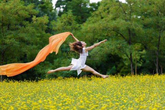 身着棕色卷发的敏捷赤脚女人在黄色野花的草地上跳跃在空中图片