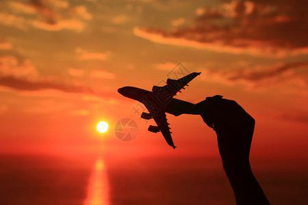 手拿着飞机缩影与日落背景的剪影背景图片