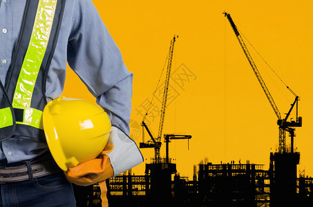 工程师在新高层公寓楼和建筑起重机的背景下为工人安全手持黄色头盔图片