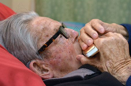 戴眼镜的老人躺在床上吹口琴图片