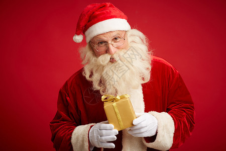 善良的圣诞老人拿着用金纸包裹的小包裹图片