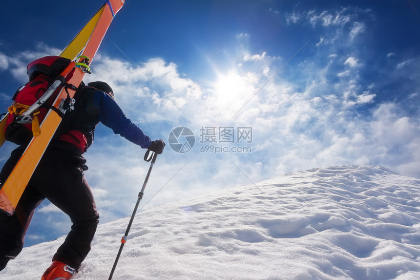 滑雪登山者带着背包里的滑雪板沿着陡峭的雪脊行走在背景中与闪亮明的太阳戏剧天空概念图片