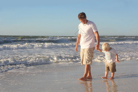 一个幼童握着他爱的父亲的手一边在海边的图片