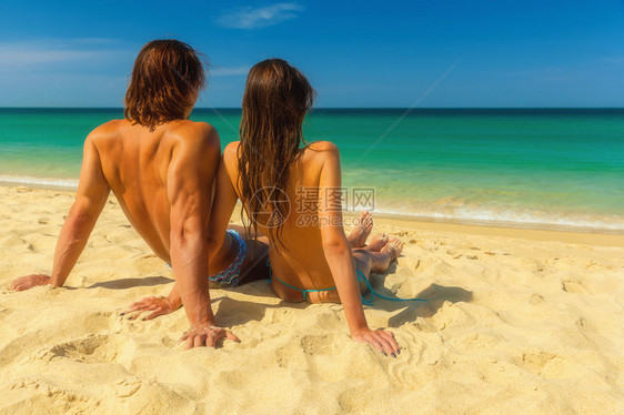 年轻一对坐在沙滩和海边坐在一起的年轻夫妇图片