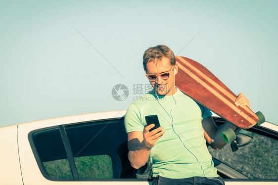 年轻的潮人在旅途中在他的车旁休息时用智能手机听音乐新趋势和现代技术的概念与复古的生活方式相结合柔和的不饱和图片
