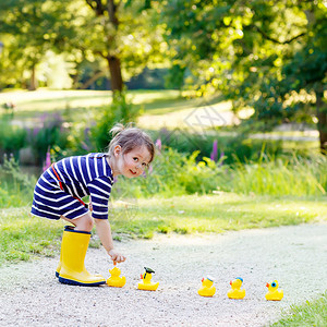 在夏日公园玩黄色橡皮鸭的黄雨靴小可爱女孩背景图片
